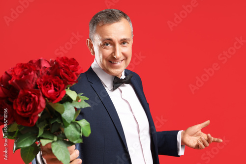 Happy mature man with bouquet of rose flowers on red background. Valentine's ...