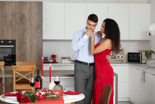 Young man kissing hand of his girlfriend near served table at home. Valentine...