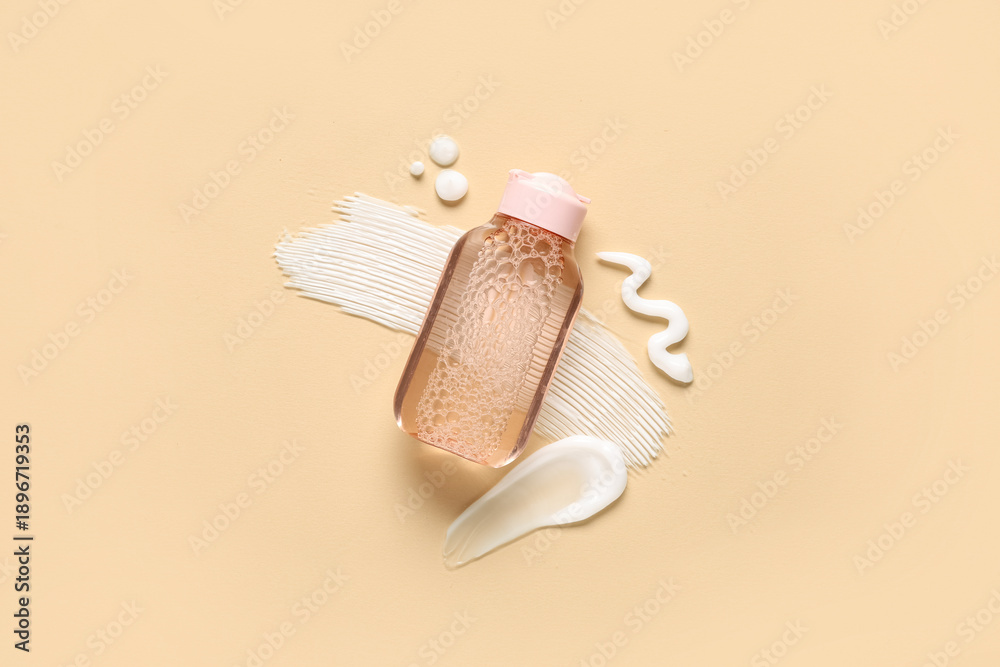 Fototapeta premium Bottle of micellar water and samples of cream on beige background