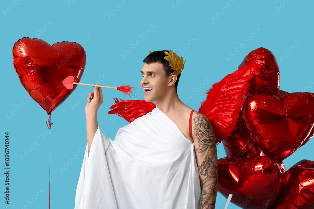 Fototapeta premium Young man dressed as Cupid with arrow and balloons on blue background. Valentine's Day celebration