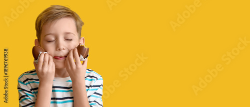 Foto Little boy with chocolate eggs licking his lips on yellow background