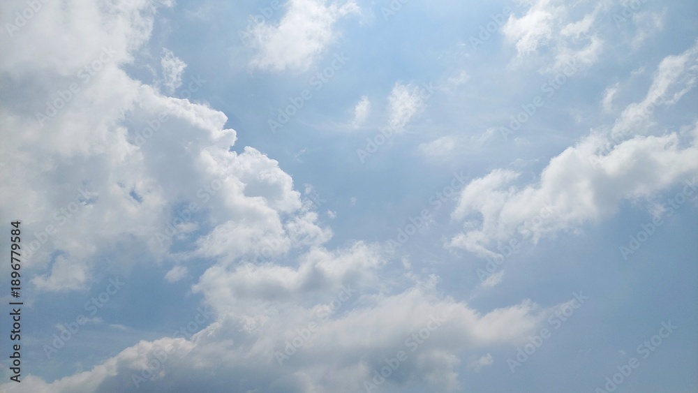 Fototapeta premium Clear blue sky with floating white clouds. Natural sky background in bright summer daylight. Beautiful blue sky texture with cloud formations.