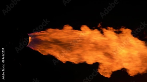 Intense orange flames erupt from a dark nozzle against a black backdrop