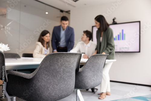 Obraz na płótnie Four professionals, analysts gathered around conference table in office, engaged in collaborative discussion, digital screen behind them displaying bar charts