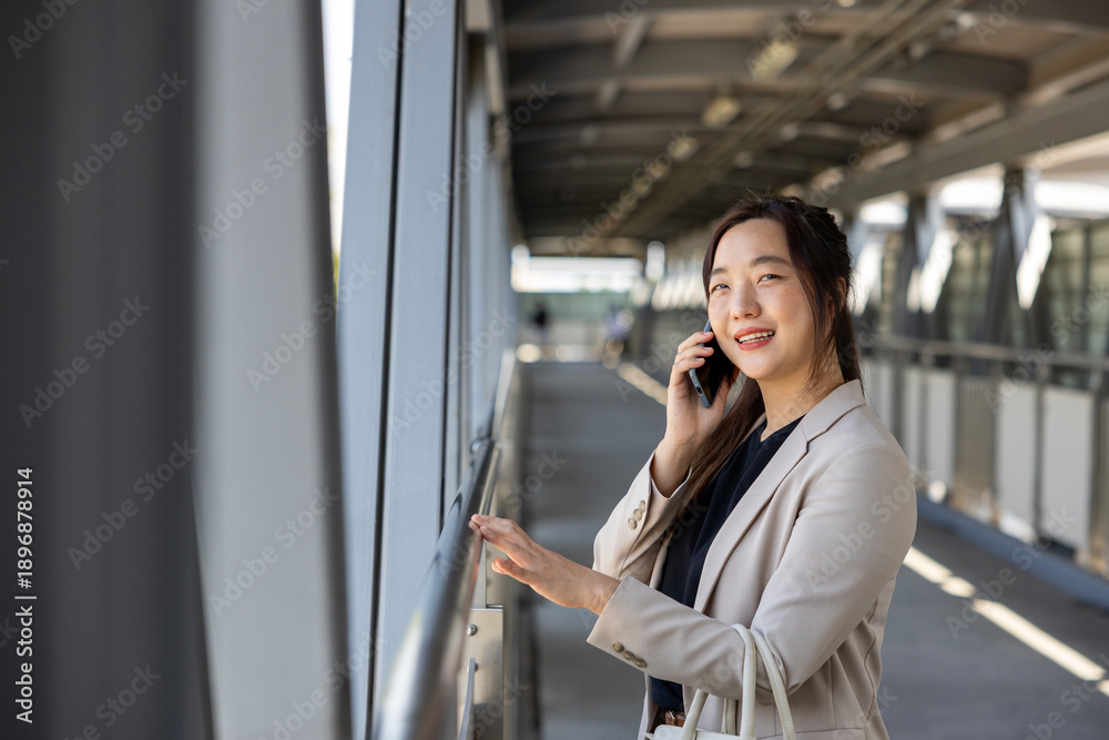 Fototapeta premium Luxury young Asian CEO woman entrepreneur using mobile phone while walking in the urban skyscraper street modern office downtown on background for business communication and urban lifestyle concept