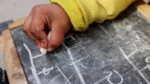 Close up of Indian village girl writing on a blackboard with chalk. Focus on education, learning and childhood in a rural mountain village of Uttarakhand, India.