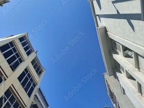 Fotografie Modern urban architecture and clear blue sky from below perspective
Low-angle view of tall city buildings under a clear blue sky, showcasing modern urban architecture and minimalistic design