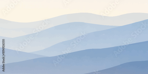 A misty mountain landscape at sunrise features snow-capped peaks and a deep valley forest partially veiled by a haze of clouds and morning fog under a soft blue sky