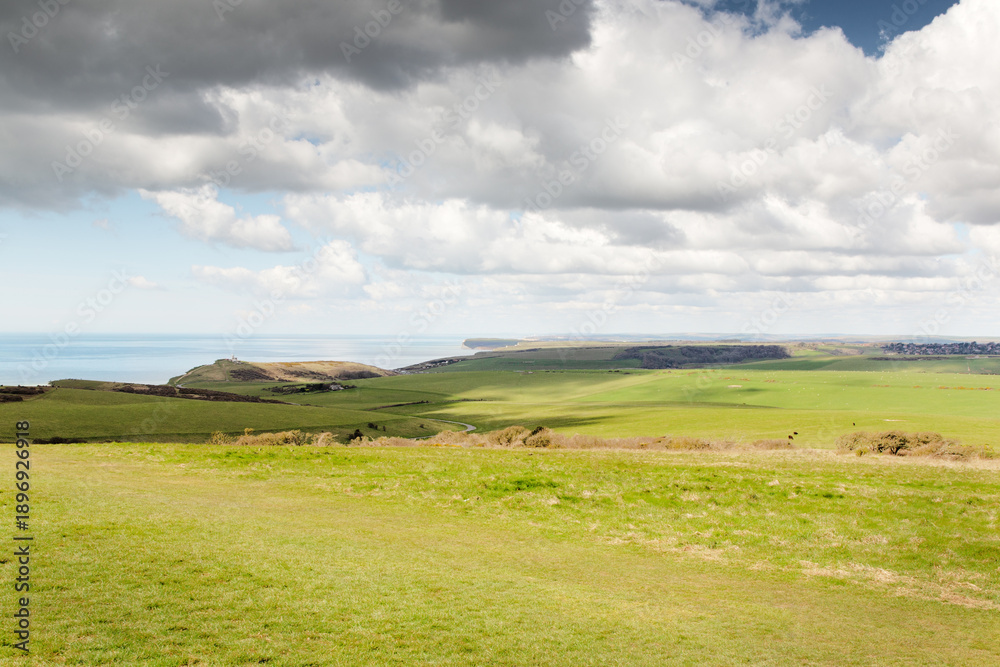 Fototapeta premium Wide Coastal Landscape With Rolling Green Fields, Sea View, And Dramatic Cloudy Sky