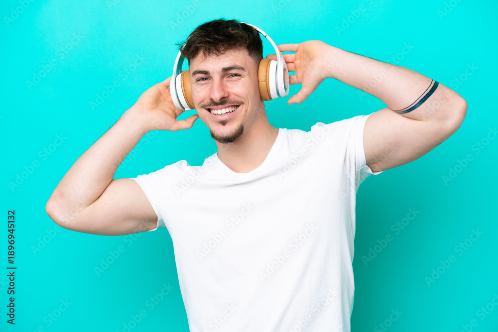 Naklejka premium Young caucasian handsome man isolated on blue background listening music
