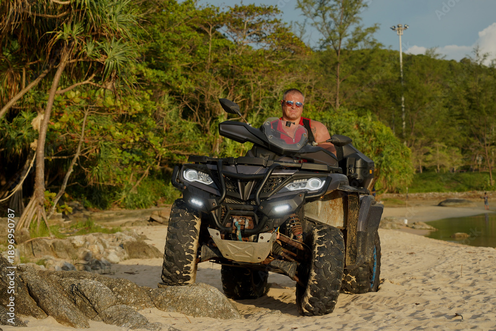 Fototapeta premium A man engages in extreme ATV riding on sand beach early in the morning