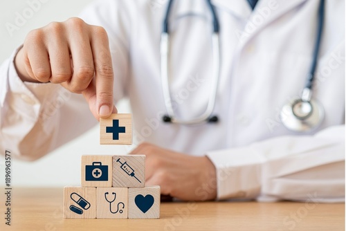 Male physician hand placing wooden block with medical cross icon on top of healthcare symbol pyramid