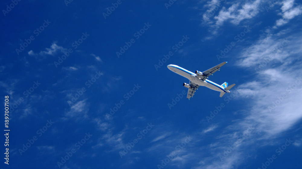 Fototapeta premium An airplane flying through a blue sky with scattered clouds.
