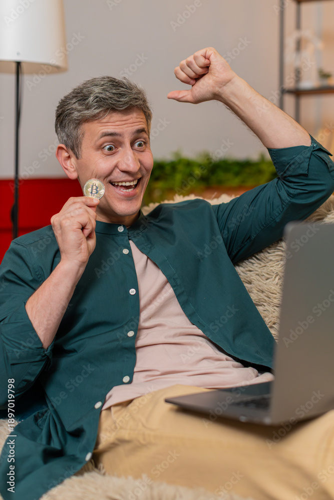 Φωτογραφία Young man at home celebrates bitcoin price surge with smile and excitement, holding coin and showing success