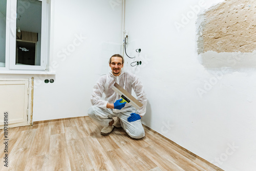Man Painting Proudly. Happy Man Finishes Painting Project. Smiling Man Shows Pride In Completed Room. Contented Man Kneels With Paint Roller In Beautifully Renovated Space