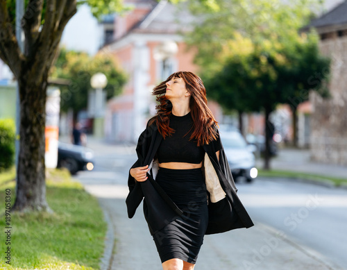 Fotografía Young woman with long brown hair, wearing a black outfit, confidently walks down