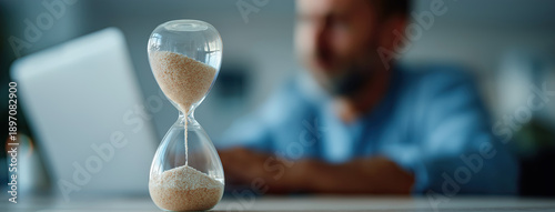 Wallpaper Mural Hourglass in foreground frames focused worker using laptop behind blur. Torontodigital.ca