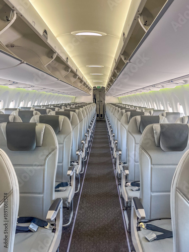 Interior view of an empty airplane cabin featuring rows of gray leather seats and overhead storage compartments, illuminated by soft ceiling lights with copy space