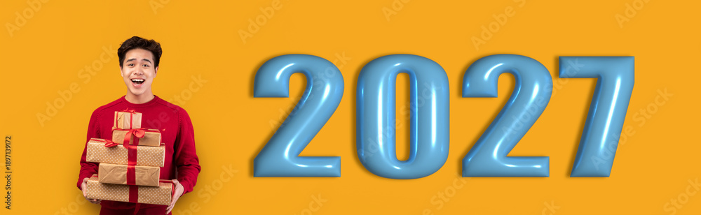 Fototapeta premium A young person stands with a stack of gifts smiling happily. The number 2027 is displayed prominently in blue against a bright yellow background. The scene shows anticipation for the new year.