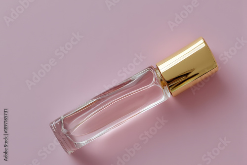 A clear perfume bottle with a gold cap on a pink background viewed from above