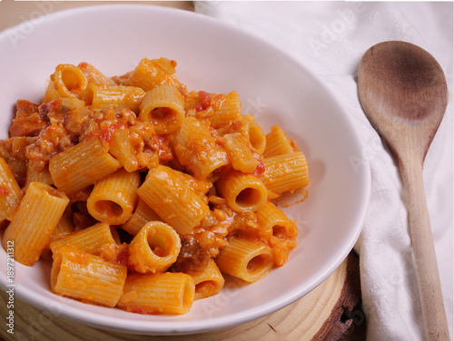 Piatto con pasta condita con pomodoro, salsiccia e guanciale