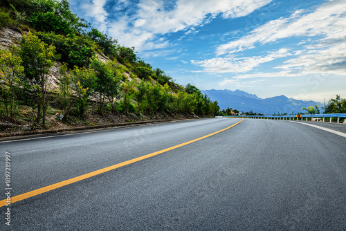 Tableau sur toile Scenic asphalt mountain road winding through green hills under a bright blue sky with white clouds
