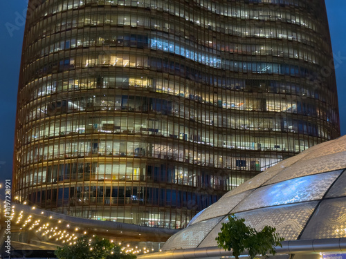 Beautiful night view of an office glass building against a unique curved roof architecture, surrounded by hanging light bulbs, and a glass dome.