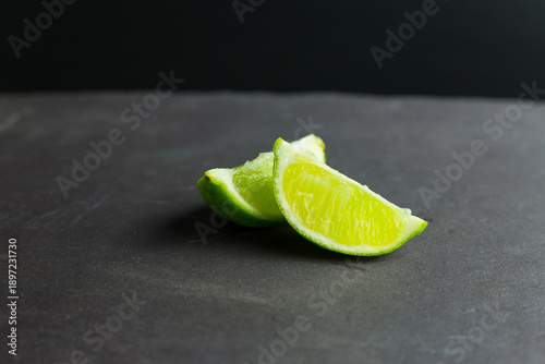 A close up image of wedges of fresh lime set on a slate grey chopping board. Concept: for use in the preparation of drinks and cocktails.