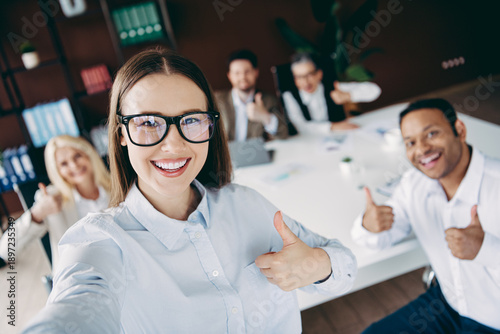 Fotografie Smiling team of coworkers showing thumbs up during an office meeting, reflecting