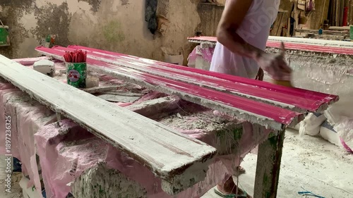 Worker painting wooden molding in a small factory in Jakarta, Indonesia. Close-up of manual manufacturing process, craftsmanship and industrial production of decorative trim in 4K resolution. December