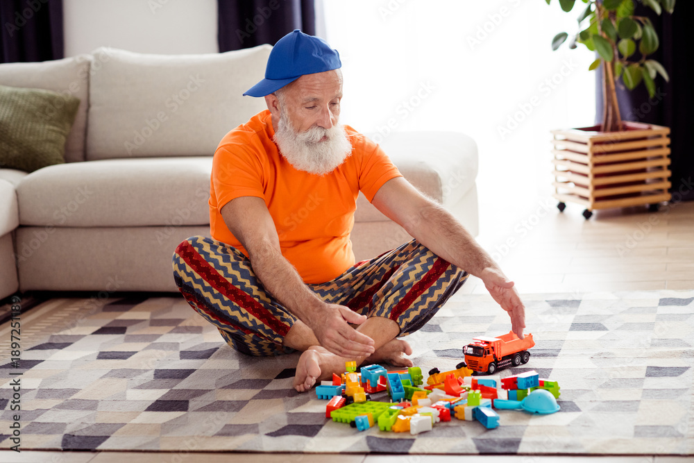 Fototapeta premium Playful grandpa in bright living room enjoys building blocks and toy truck indoors on a cozy weekend at home