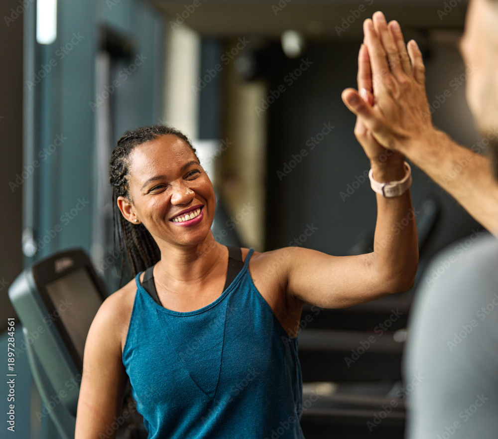 Fototapeta premium Portrait of a young black woman and white man trainer instructor exercising in a gym, celebrating success running using thereadmill machine equipment, healthy lifestyle and cardio exercise and teamwor
