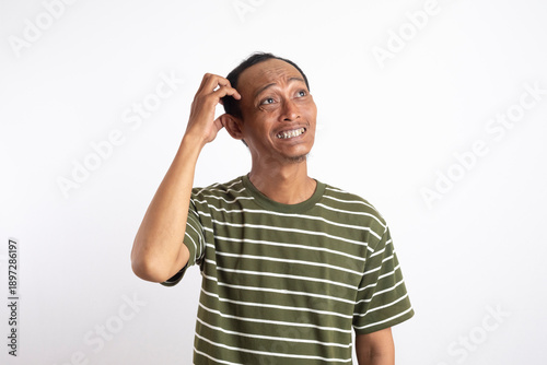 Foto Confused Asian man scratching his head while looking up with an awkward smile