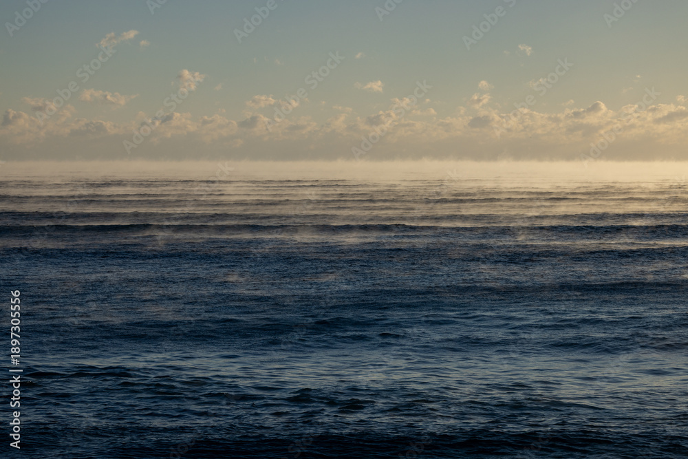 Fototapeta premium Cold Morning Ocean with Sea Smoke and Soft Clouds at Sunrise