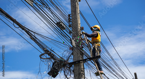 Technician working at height on a chaotic tangle of fiber optic and electrical lines using a ladder.