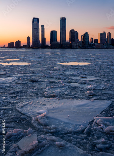 Frozen Hudson River with drifting ice floes facing Downtown Jersey City skyscrapers, New Jersey, during an winter freeze at twilight