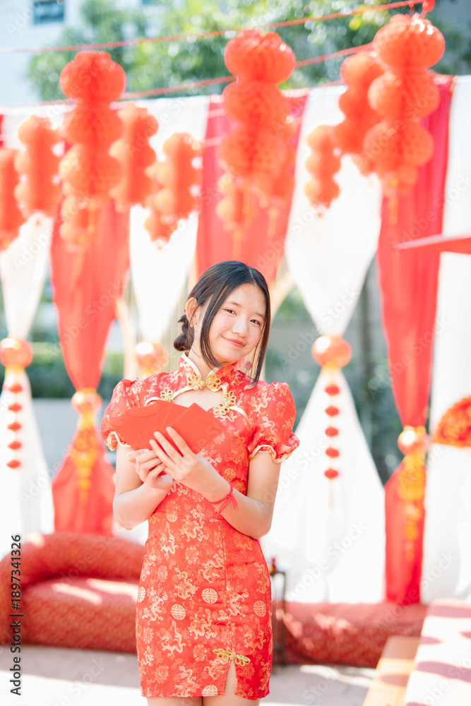 Obraz premium The celebration of Chinese New Year traditions: a young woman in a red qipao (traditional Chinese dress) holding a red envelope.