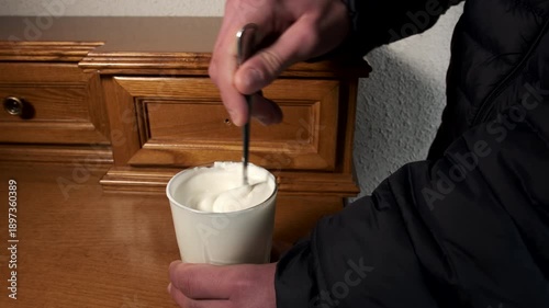 Male hand mixing creamy white yogurt with spoon