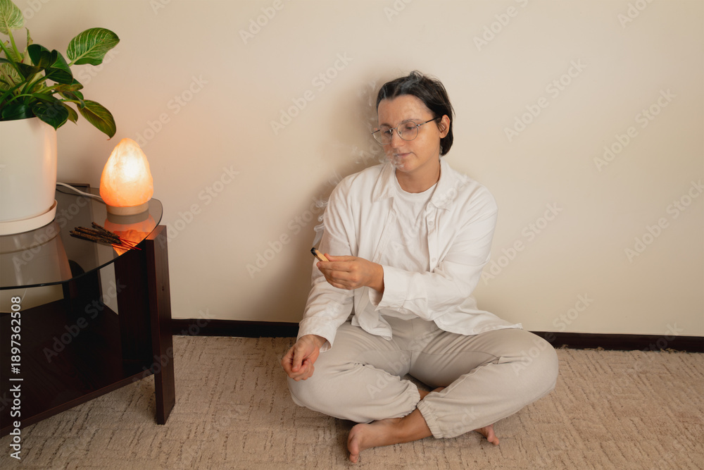 Fototapeta premium Young caucasian female meditating indoors with incense and salt lamp