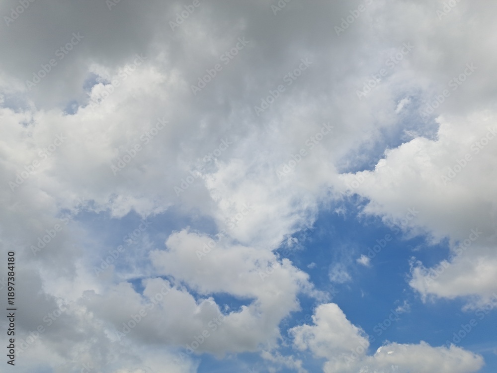 Obraz premium Afternoon sky filled with clouds, illuminated by the bright afternoon sun – White and grey clouds illuminated by the rays of the afternoon sun, amidst a blue sky.