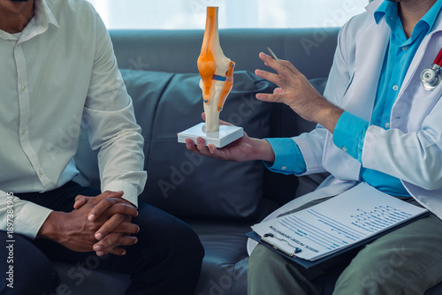 Tableau sur toile The doctor is providing consultation and treatment for a patient with knee pain, using a bone model, and also recommending preventive measures and health care to alleviate knee pain