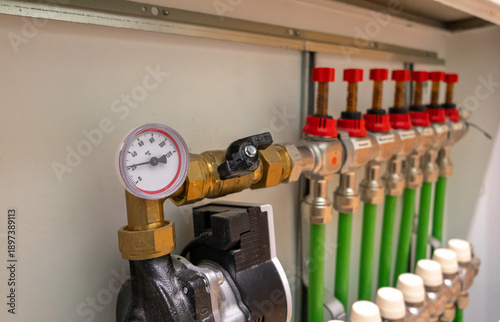Foto A modern domestic hydronic underfloor heating manifold with pipes, valves, flow meters, and a circulation pump