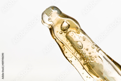 Macro of pipette with liquid yellow gel with bubbles on light background.