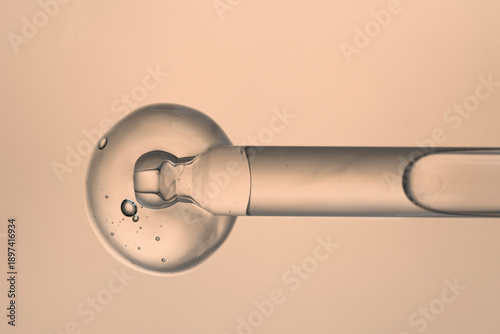 Pipette with clear liquid and a drop of serum on a beige background, top view.