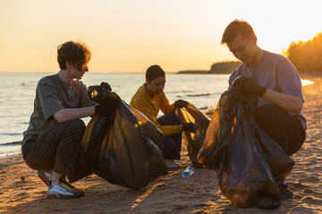 Earth day. Volunteers activists team collects garbage cleaning of beach coastal zone. Woman mans puts plastic trash in garbage bag on ocean shore. Environmental conservation coastal zone cleaning