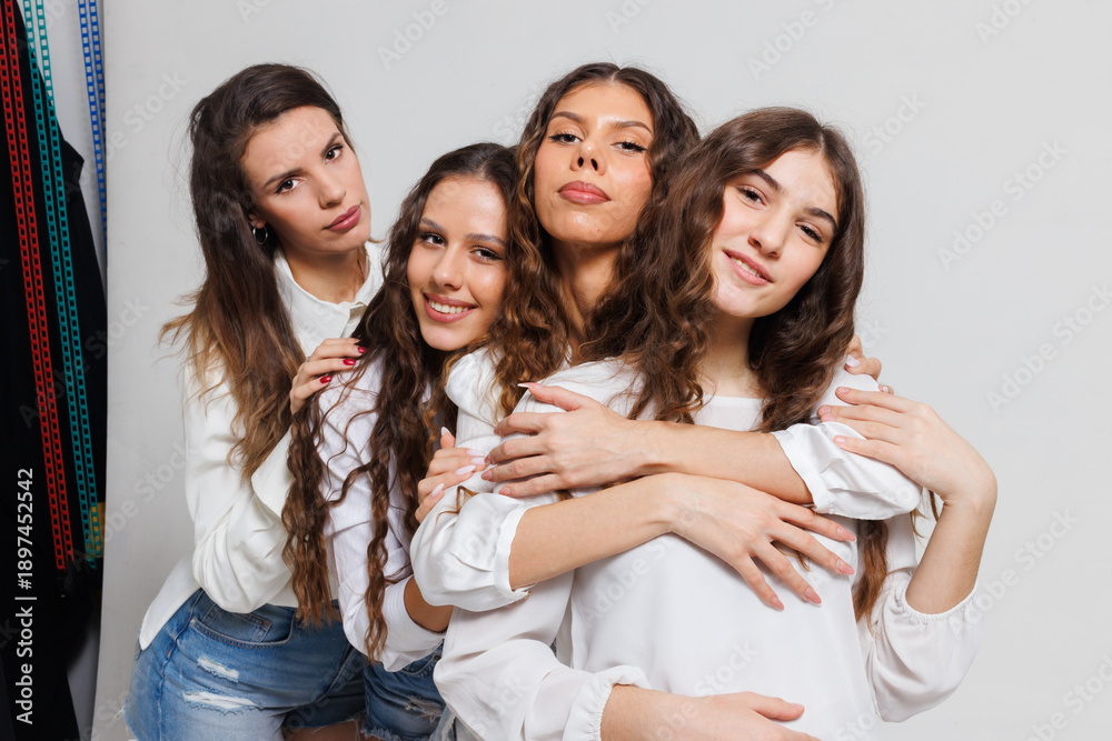 Obraz premium Group of four young women posing cheerfully and embracing each other in a studio setting