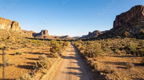 Dusty Desert Trail Winds Through Rugged Arid Landscape Under Clear Blue Sky Bathed in Golden Hour Sunlight