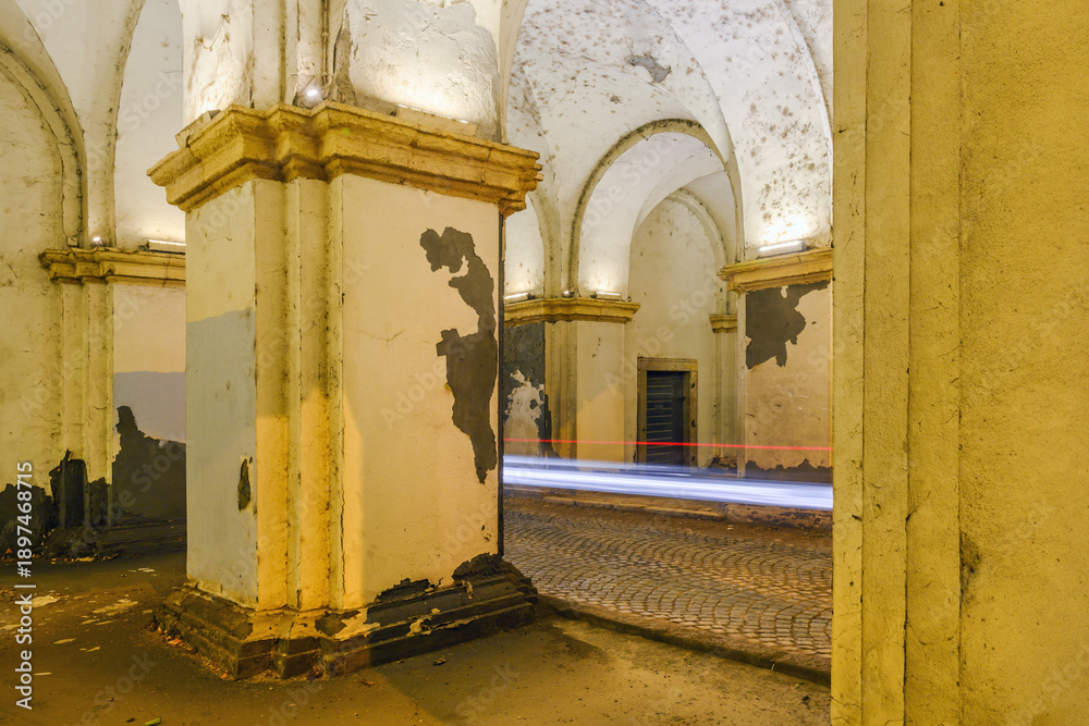 Fototapeta premium Abandoned arched corridor with peeling paint and car light trails, long exposure