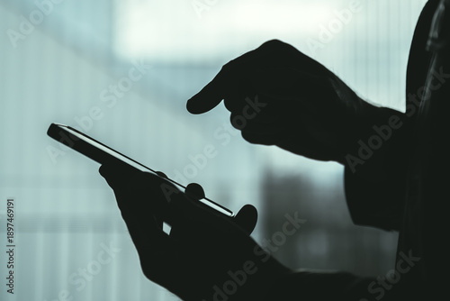 Silhouette of male hands using smartphone indoors, anonymous profile expressing privacy, technology use, communication, or digital dependence.