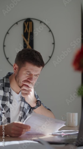 Wallpaper Mural Man sitting at desk at home checking utility bills and financial papers with laptop. Concept of high household expenses, budgeting and financial stress. Torontodigital.ca
